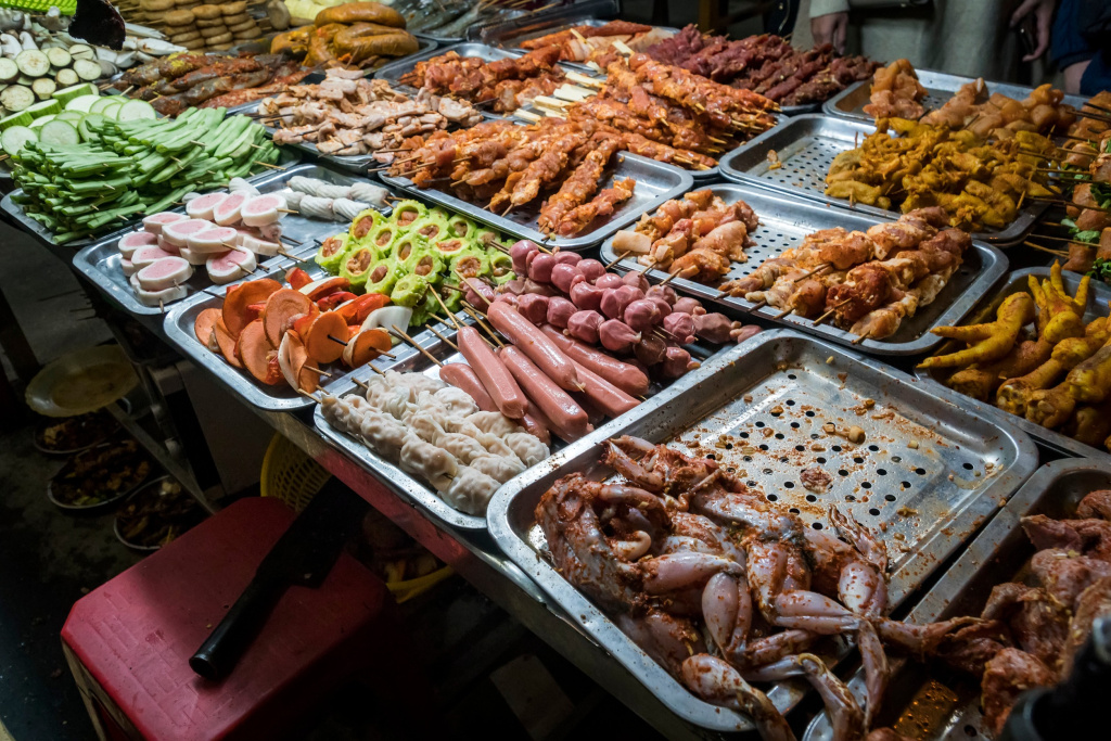 Уличный рынок с вьетнамской кухней в Ханое. Сырая курица, лягушки и овощи на подносах для гриля