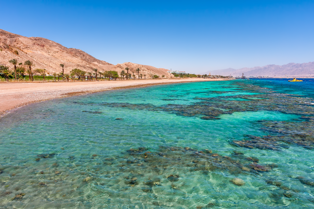 Лазурная вода и подводные кораллы вдоль пустого пляжа на популярном курорте Эйлат на Красном море в Израиле